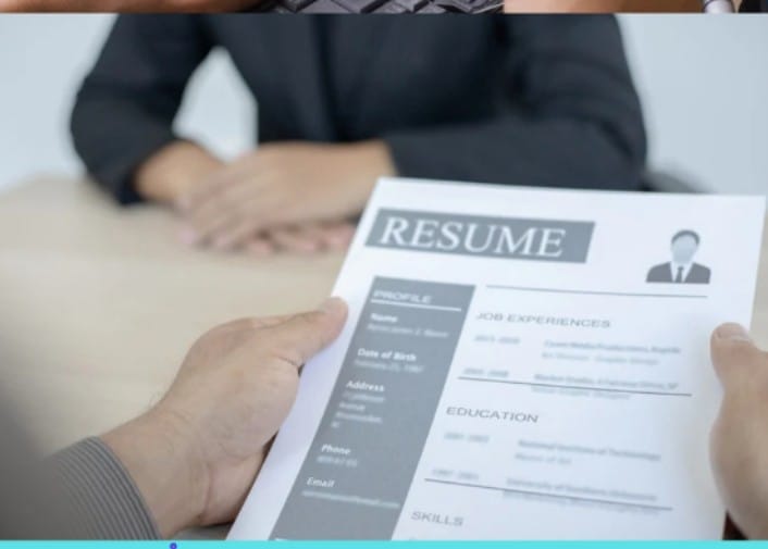 A person holding a resume with sections for Profile, Job Experiences, Education, and Skills in front of another person sitting at a table.