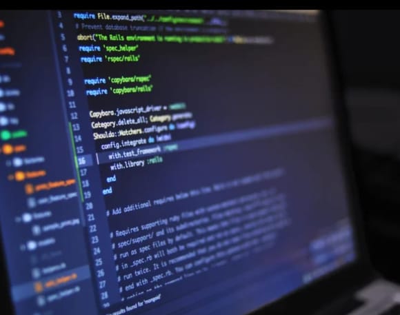 A laptop screen displaying lines of code in Ruby programming language with syntax highlighting in green, white, and orange on a dark background.