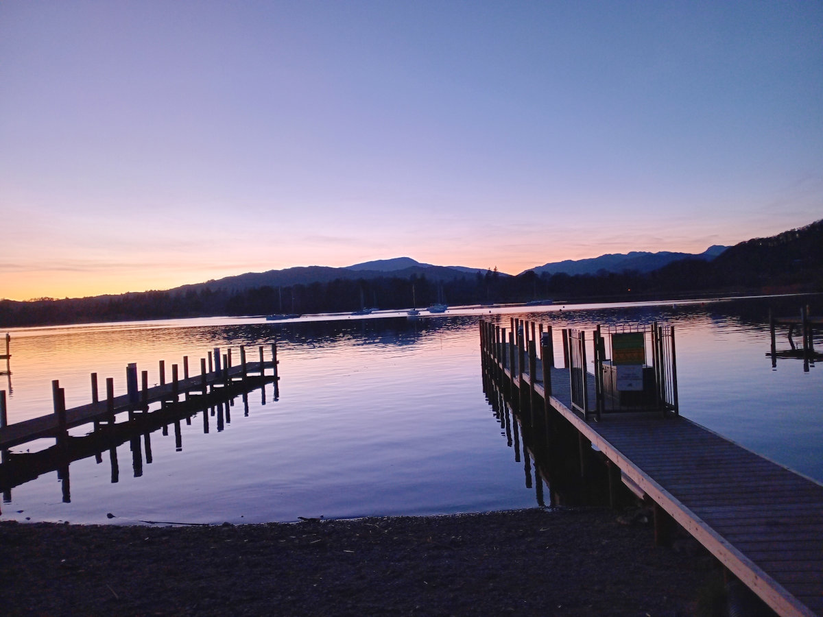 Sunset scene overlooking a lake with sun reflecting in the water and mountains in distance.