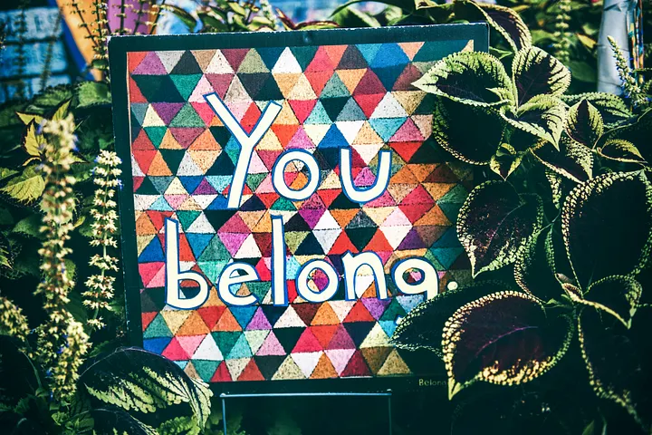 A colorful sign saying "You Belong" with plants surrounding it.