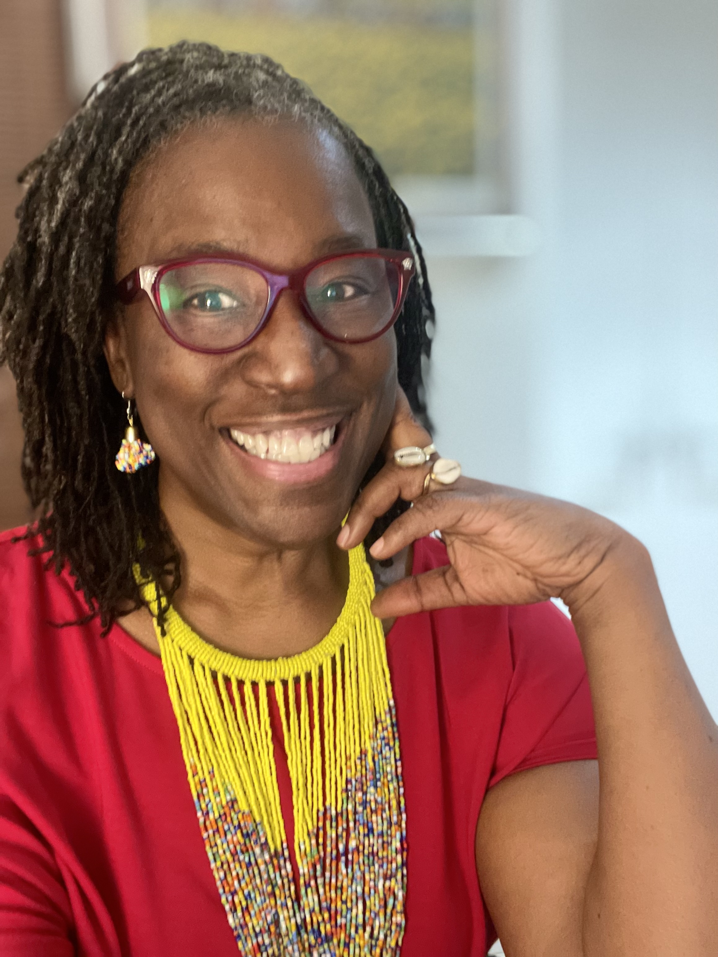 Scarlet Ibis James is radiant, smiling widely in a red top with yellow statement necklace.