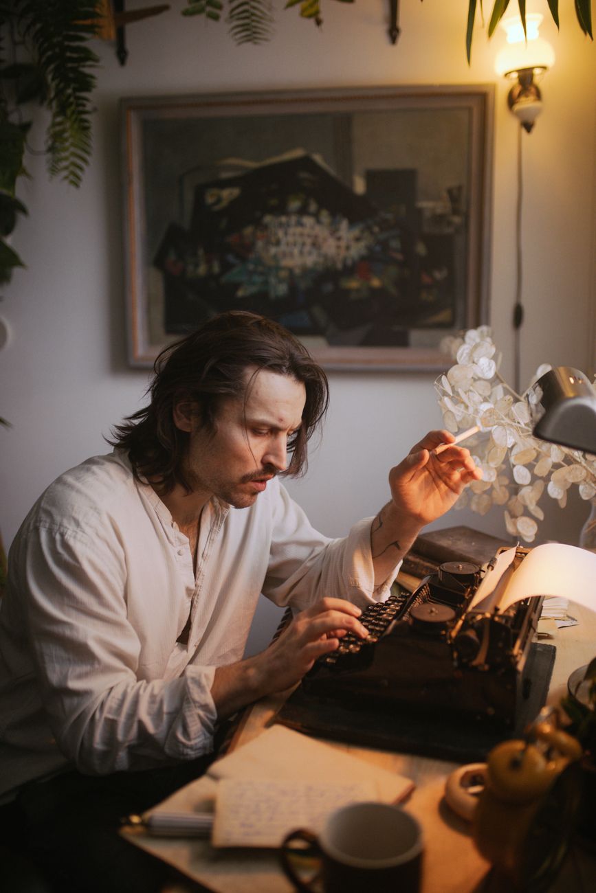 a man in white long sleeve shirt sitting at the table using a typewriter